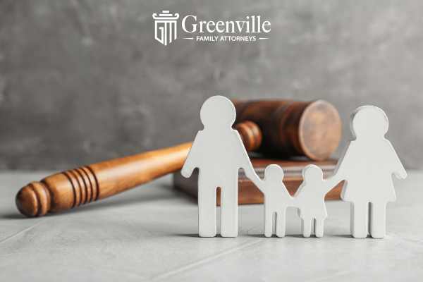 a cut out of two parents and two children and a gavel on a white desk